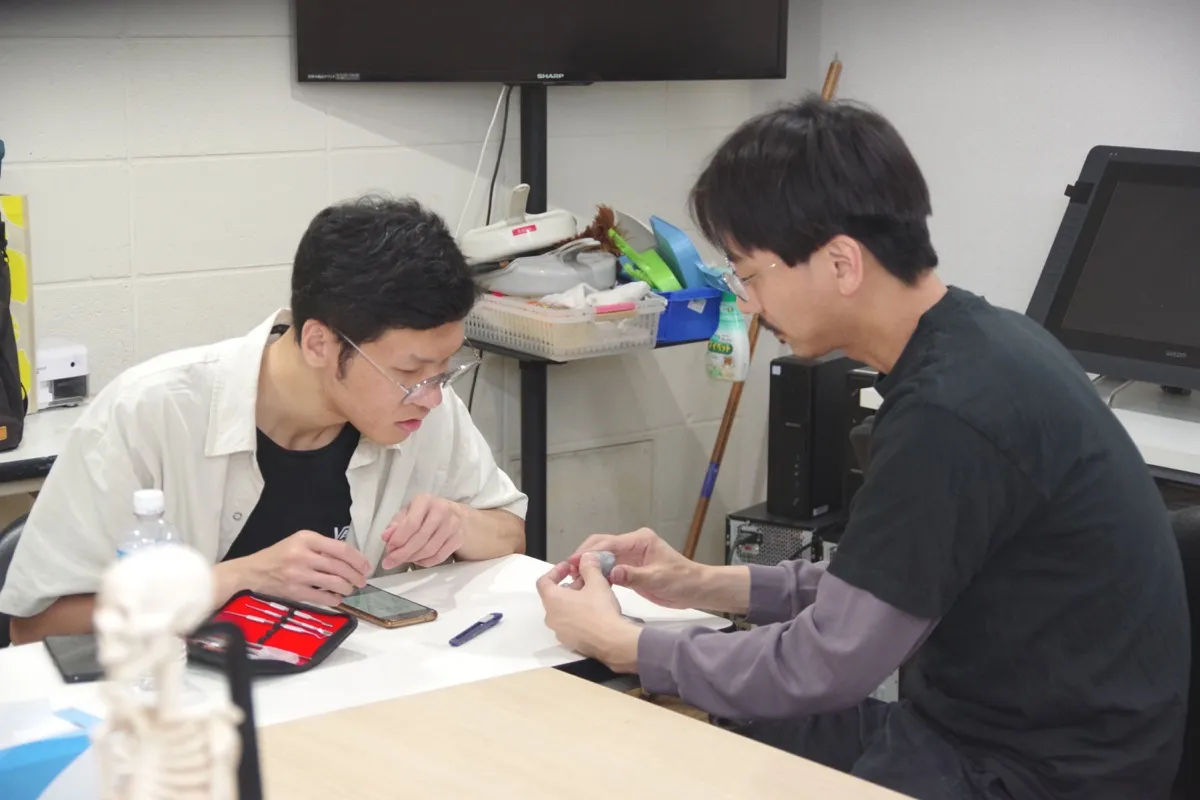 先生が学生のすぐとなりで絵にアドバイスしている授業の様子